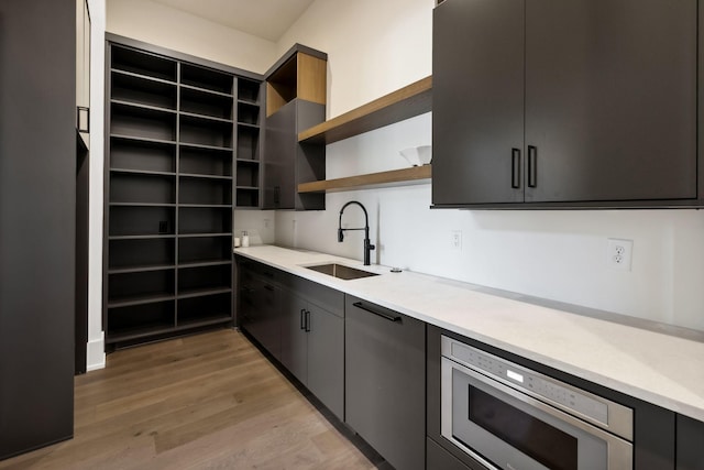 kitchen with stainless steel microwave, light countertops, light wood-type flooring, open shelves, and a sink