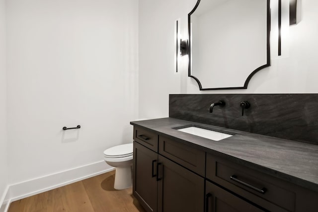 bathroom featuring toilet, baseboards, wood finished floors, and vanity