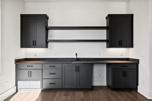 kitchen with open shelves, dark wood-style flooring, dark countertops, and a sink