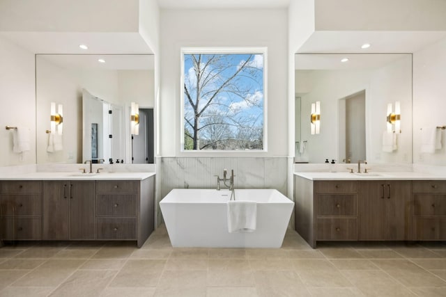 bathroom featuring a freestanding tub, recessed lighting, a sink, and wainscoting