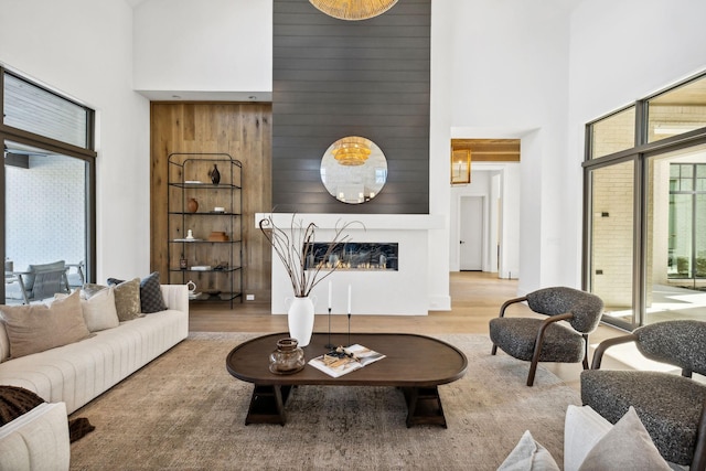 living area with a glass covered fireplace, a towering ceiling, and wood finished floors