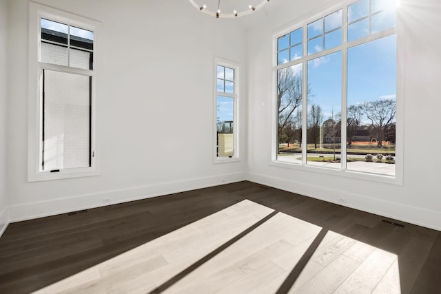 unfurnished room with a chandelier, dark wood-type flooring, visible vents, and baseboards