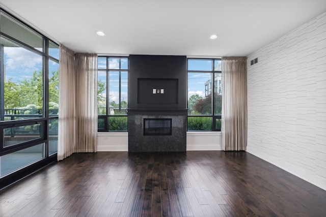 unfurnished living room with dark wood-type flooring, a glass covered fireplace, visible vents, and plenty of natural light