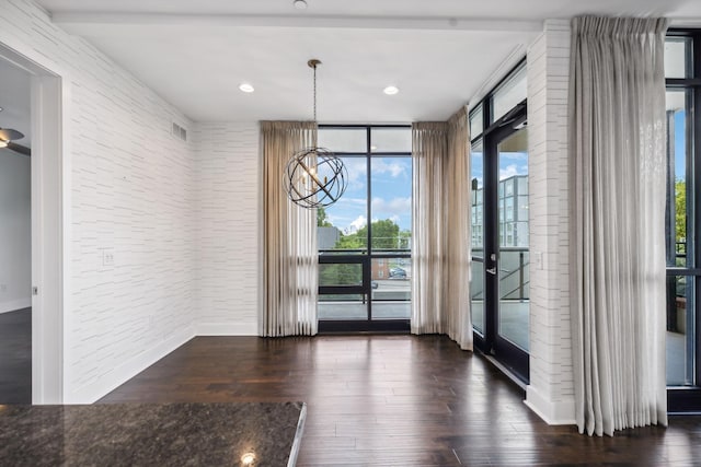 unfurnished dining area featuring brick wall, floor to ceiling windows, a chandelier, and dark wood-style flooring