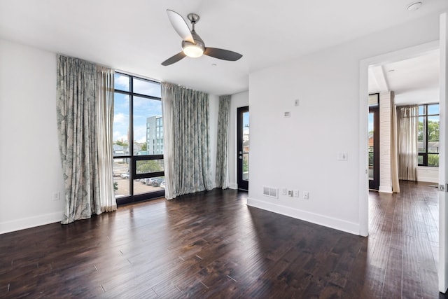 unfurnished room with floor to ceiling windows, dark wood finished floors, visible vents, ceiling fan, and baseboards