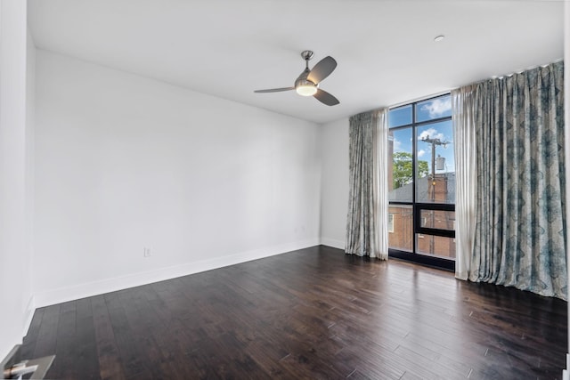 spare room with dark wood-style floors, expansive windows, baseboards, and a ceiling fan