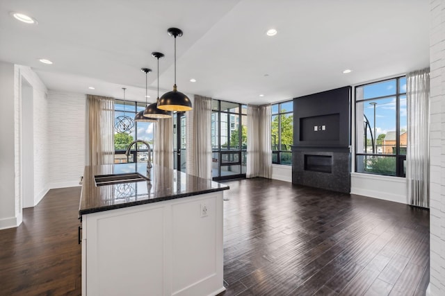 kitchen featuring a large fireplace, a center island with sink, dark stone counters, pendant lighting, and a sink