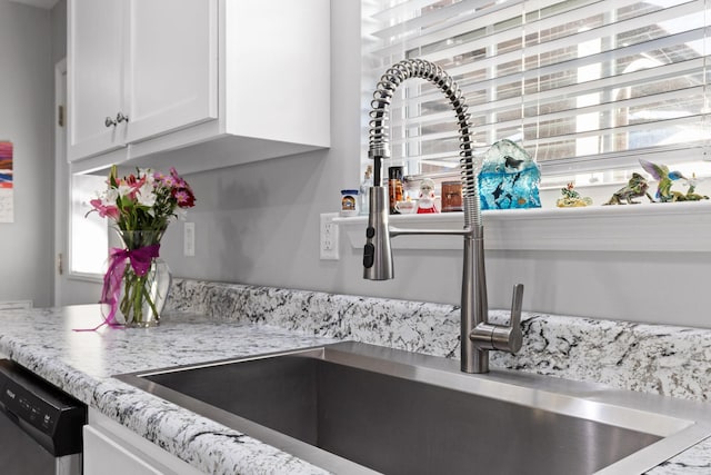 kitchen with a sink, white cabinetry, light stone counters, and stainless steel dishwasher