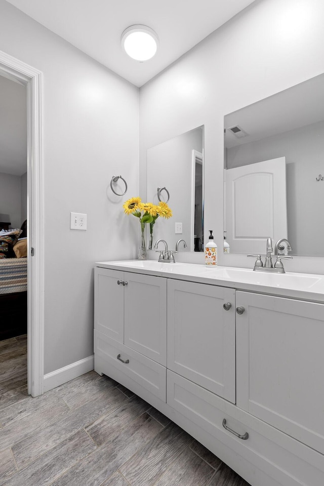 ensuite bathroom featuring double vanity, connected bathroom, a sink, wood finished floors, and baseboards