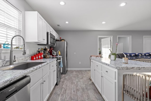 kitchen with recessed lighting, appliances with stainless steel finishes, white cabinetry, a sink, and light wood-type flooring