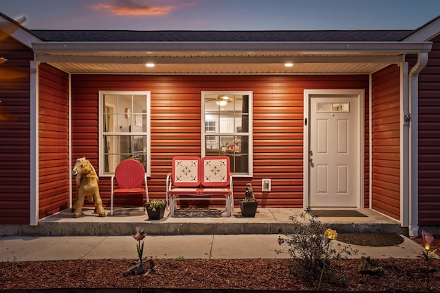 exterior entry at dusk featuring covered porch and roof with shingles