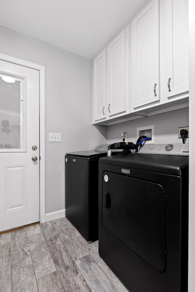 clothes washing area with cabinet space, washing machine and dryer, baseboards, and light wood finished floors