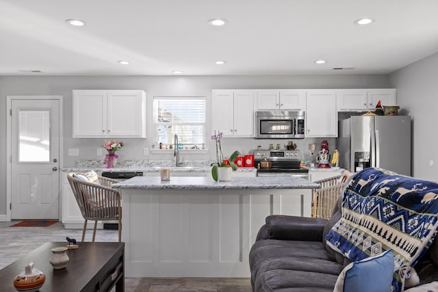 kitchen with stainless steel appliances, recessed lighting, white cabinetry, and light stone counters