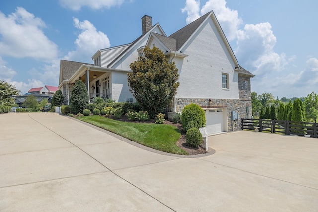 view of home's exterior with driveway, stone siding, an attached garage, and fence