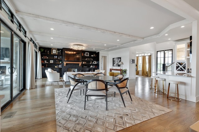 dining room with light wood-style floors, a brick fireplace, beamed ceiling, and recessed lighting