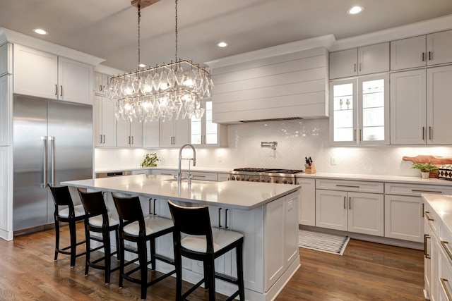 kitchen featuring stainless steel appliances, white cabinets, light countertops, wall chimney exhaust hood, and an island with sink