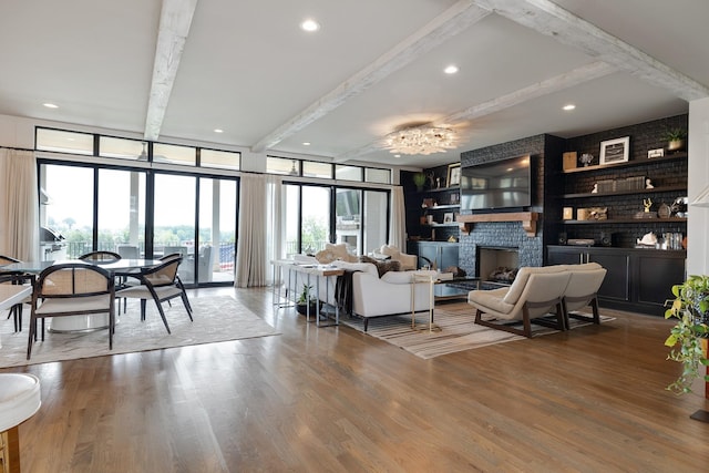 living area featuring beam ceiling, a fireplace, recessed lighting, wood finished floors, and a wall of windows