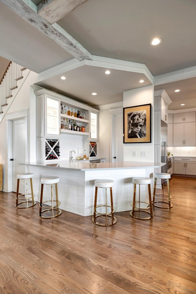 bar with built in refrigerator, light wood-style floors, indoor wet bar, and recessed lighting