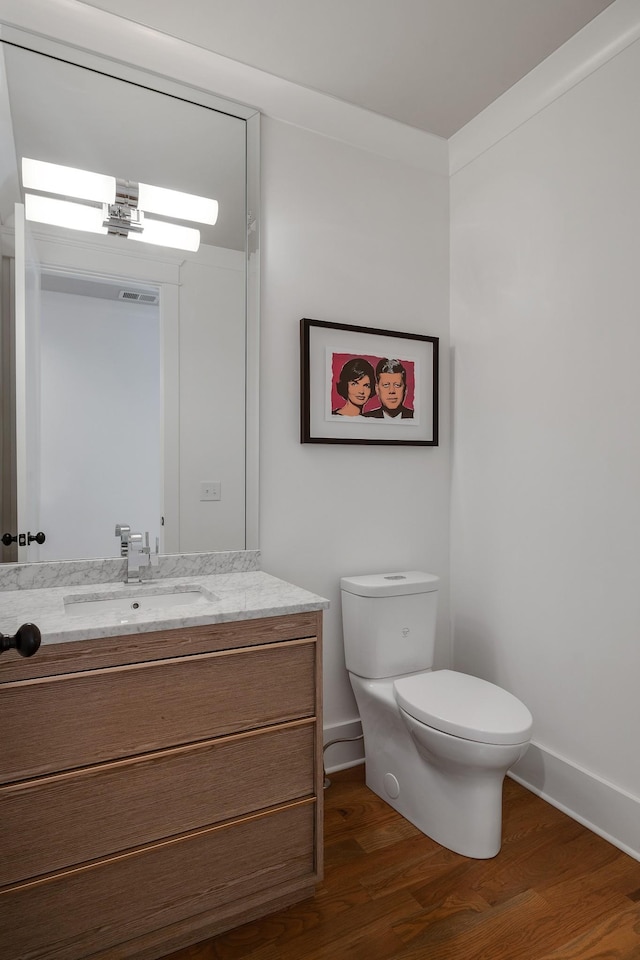 half bath featuring visible vents, baseboards, toilet, wood finished floors, and vanity