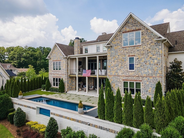 back of property with stone siding, a patio area, an outdoor pool, and a balcony