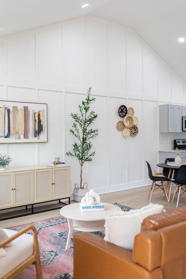 living room featuring light wood-type flooring, vaulted ceiling, a decorative wall, and recessed lighting