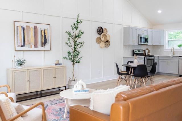 living area featuring lofted ceiling, light wood-style floors, a decorative wall, and recessed lighting