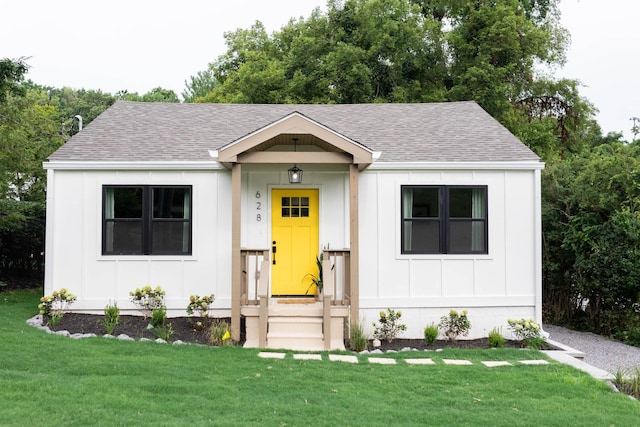 view of front of property with board and batten siding, a front yard, and roof with shingles