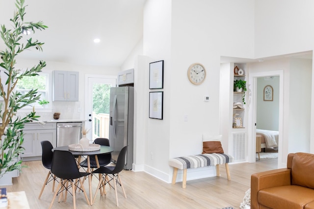 dining room with high vaulted ceiling, light wood finished floors, and baseboards