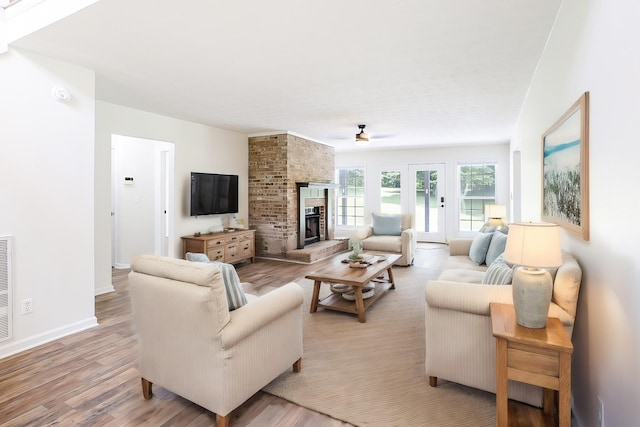 living room featuring light wood finished floors, ceiling fan, a fireplace, and baseboards