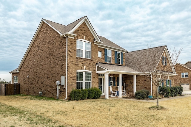 view of front of house with a shingled roof, brick siding, fence, and a front lawn