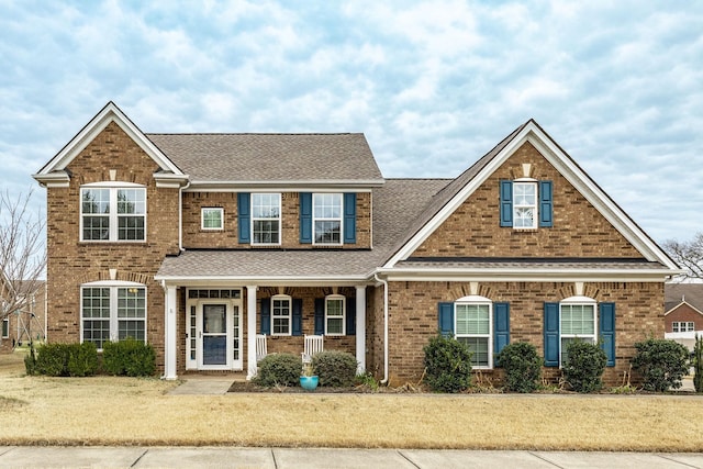 view of front of house featuring a shingled roof, a front yard, and brick siding