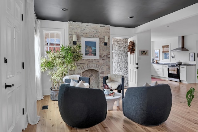 living area with a brick fireplace, light wood-style flooring, and visible vents