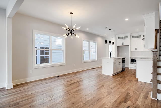 kitchen featuring light countertops, decorative backsplash, a sink, light wood finished floors, and beverage cooler