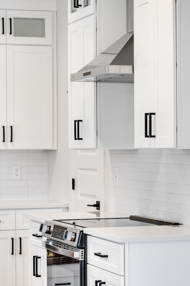 kitchen featuring light countertops, wall chimney range hood, stainless steel electric range oven, and white cabinets
