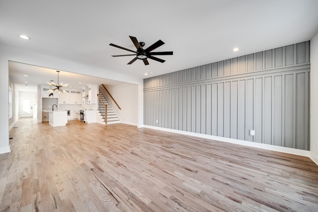 unfurnished living room with recessed lighting, stairs, light wood-type flooring, a sink, and ceiling fan with notable chandelier