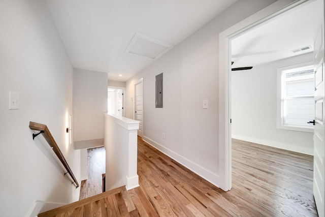 hall with an upstairs landing, light wood-style flooring, visible vents, baseboards, and attic access
