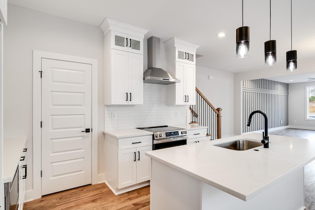 kitchen featuring light wood-style flooring, stainless steel range with electric cooktop, a sink, wall chimney range hood, and backsplash