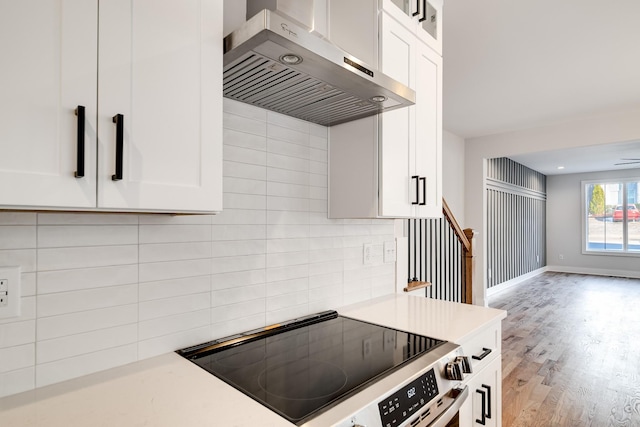 kitchen featuring wall chimney exhaust hood, range, and white cabinets