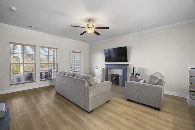 living room with light wood finished floors, visible vents, ornamental molding, a ceiling fan, and baseboards