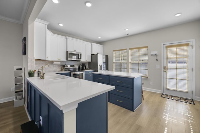 kitchen featuring white cabinets, blue cabinets, appliances with stainless steel finishes, and light countertops