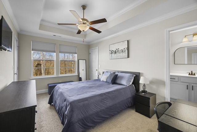 bedroom featuring light carpet, baseboards, ornamental molding, a raised ceiling, and ensuite bath