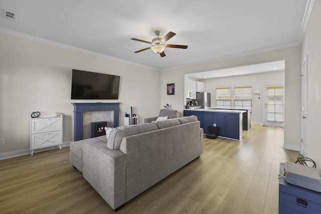 living area with a lit fireplace, ornamental molding, wood finished floors, and visible vents