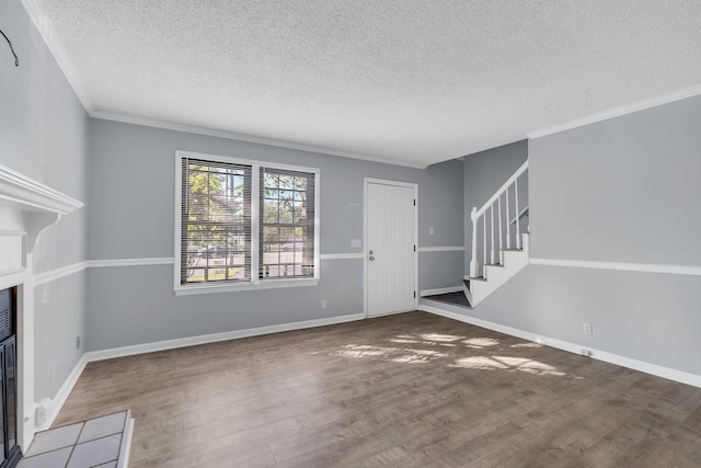 unfurnished living room with stairs, ornamental molding, a tiled fireplace, and wood finished floors