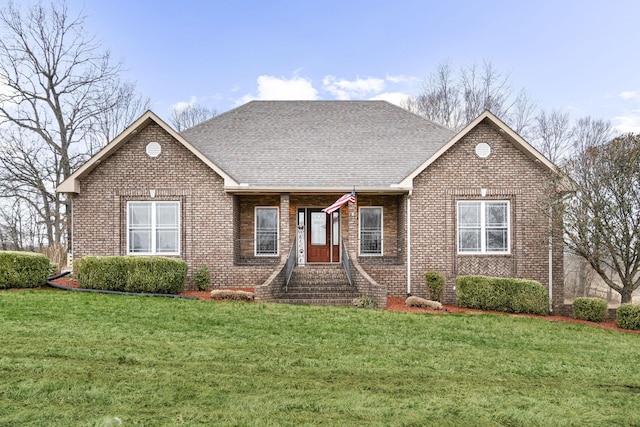 single story home featuring a shingled roof, a front yard, and brick siding