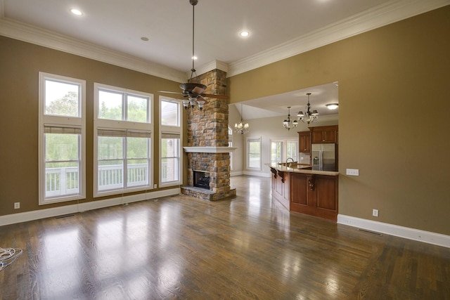 unfurnished living room featuring baseboards, dark wood-style floors, ornamental molding, a stone fireplace, and ceiling fan with notable chandelier