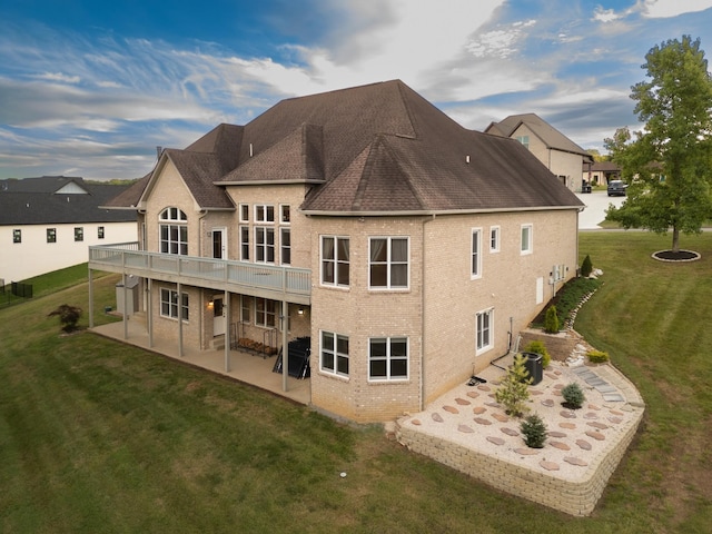 back of property with brick siding, a shingled roof, a lawn, and a patio