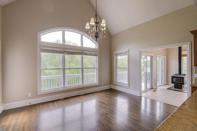 unfurnished living room with a wood stove, baseboards, high vaulted ceiling, and wood finished floors