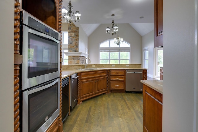 kitchen with a chandelier, stainless steel appliances, a sink, brown cabinets, and pendant lighting