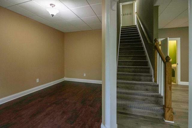 stairway featuring a paneled ceiling, baseboards, and wood finished floors