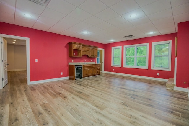 interior space with light wood-type flooring, beverage cooler, baseboards, and bar area